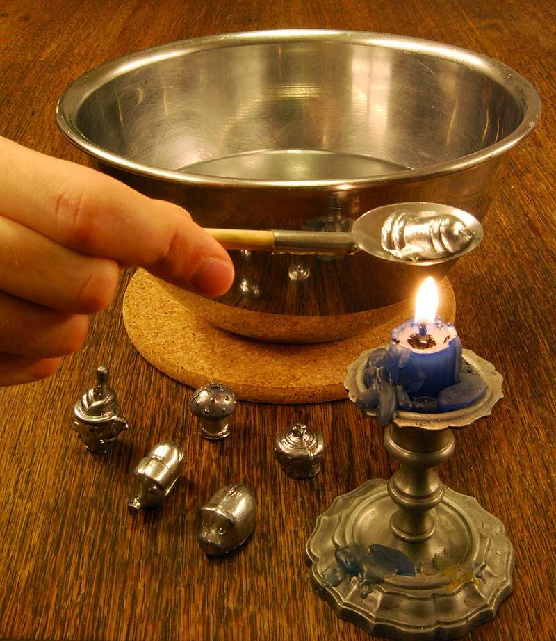 Lžička s roztaveným olovem nad svíčkou a miska s vodou v pozadí na stole