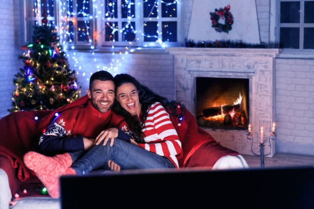 Pár, sledující televizi v místnosti vyzdobené vánočními světýlky.