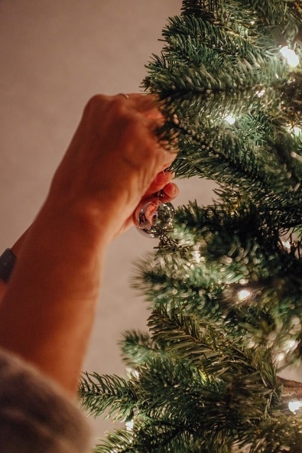 Detail na ruce zdobící vánoční stromeček se světýlky. 
