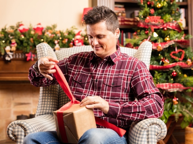 Muž rozbalující si vánoční dárek s červenou stuhou.