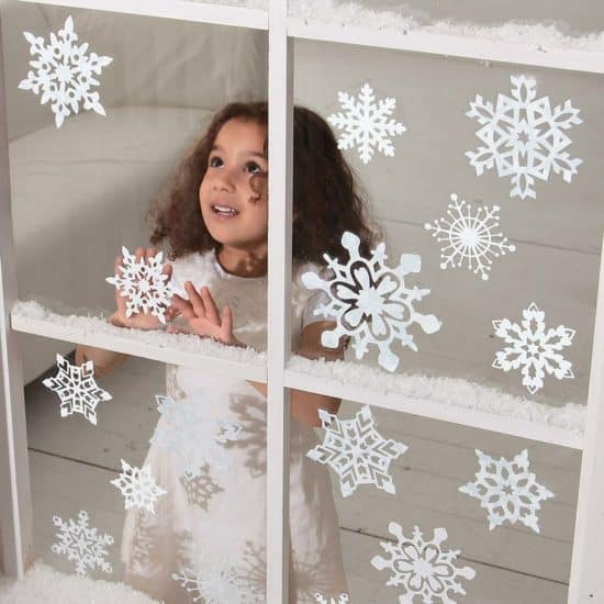 Holčička za oknem polepeným papírovými vánočními vystřihovánkami ve tvaru sněhových vloček