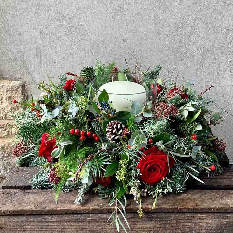 Vánoční aranžmá z větviček, šišek a květin se svíčkou jako dekorace na hrob