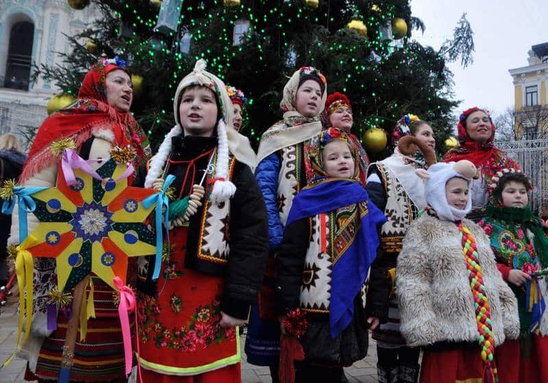 Děti v tradičních ukrajinských krojích zpívající koledy u stromečku.