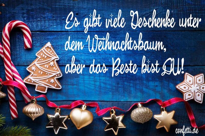 Text vánočního přání v němčině na modrém dřevě, ozdobeném perníky, hůlkami a ozdobami na červené stužce