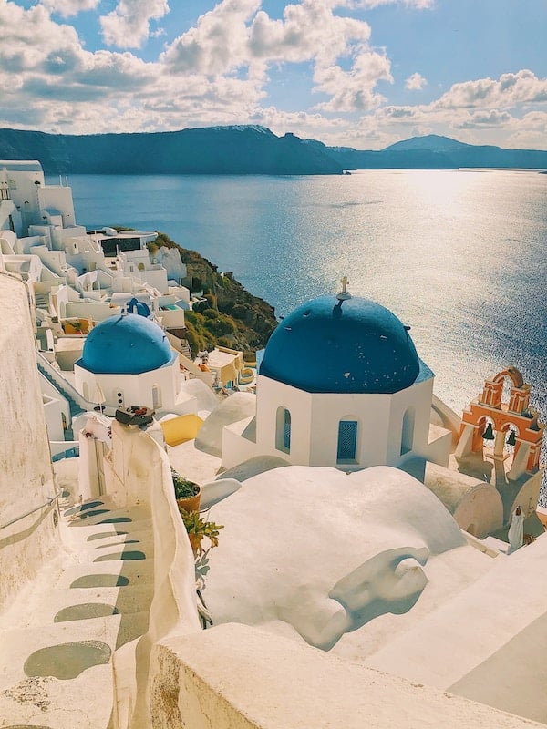 Řecké Santorini a jeho krásné modré střechy na bílých budovách, v dálce sluncem osvícené moře.