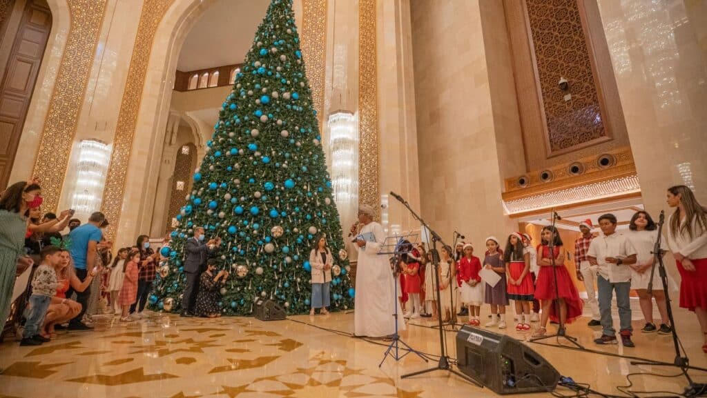 Velký vánoční strom a skupina zpívajících dětí.