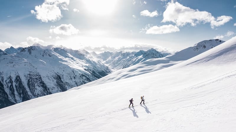 Dvojice kráčí k vrcholu zasněženou planinou.
