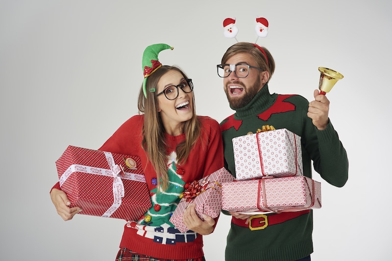 Muž a žena se smějí, přitom jsou humorně odění do vánočního, se spoustou ozdob, nesou dárky.