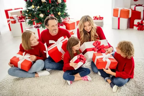 Rodina sedící u vánočního stromečku otevírající dárky.